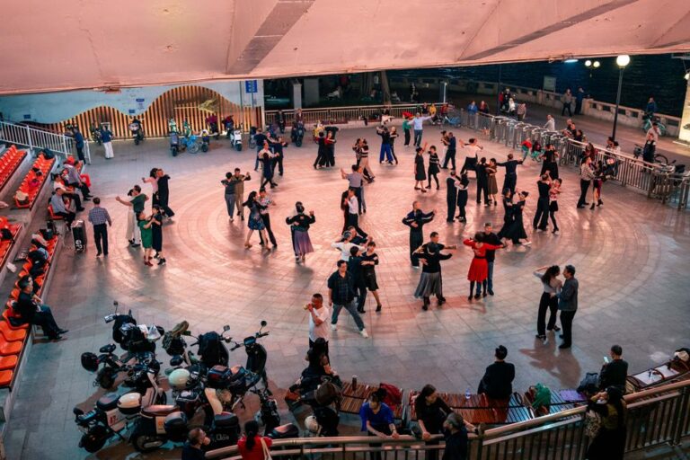 Couples and individuals dance on a wooden floor under string lights, wearing jeans and boots.