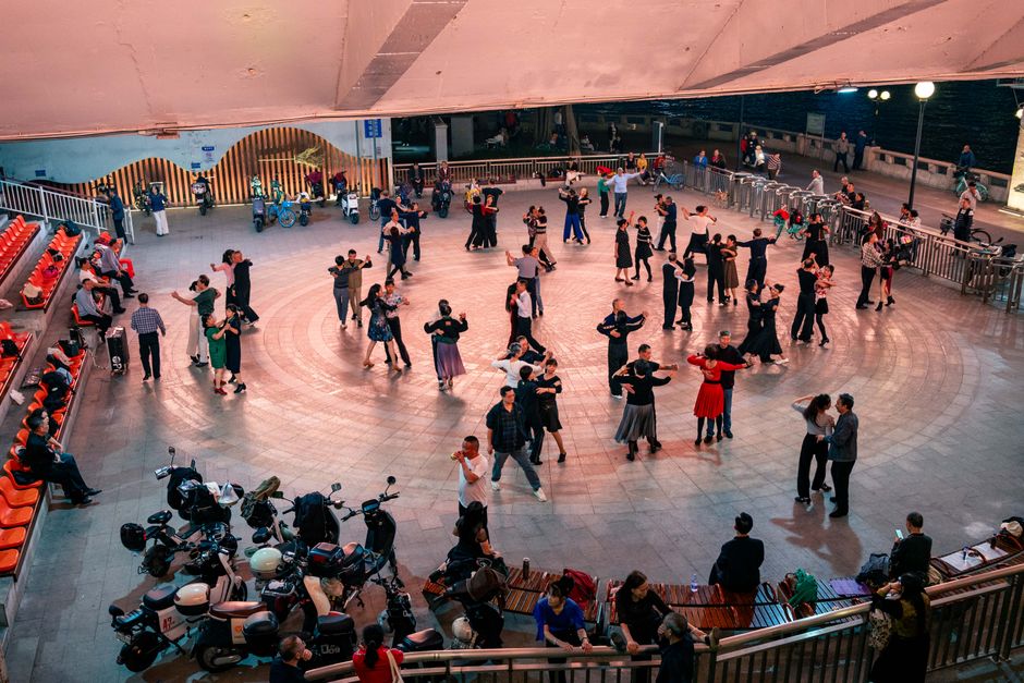 Couples and individuals dance on a wooden floor under string lights, wearing jeans and boots.