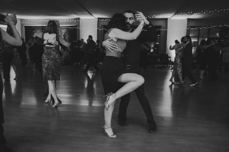 A couple dancing together on a wooden dance floor under string lights in a lively hall.