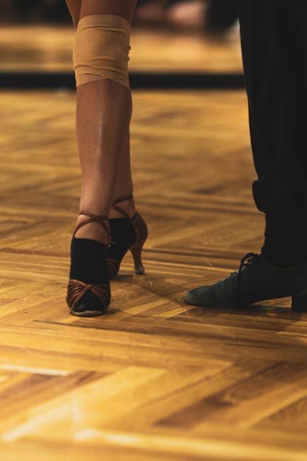 Beginner dancers practicing simple steps on a wooden dance floor while others move nearby